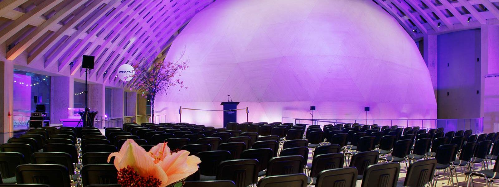 en rund dome som visas i bakgrunden upplyst av lila. Framför finns svarta stolar uppradade.