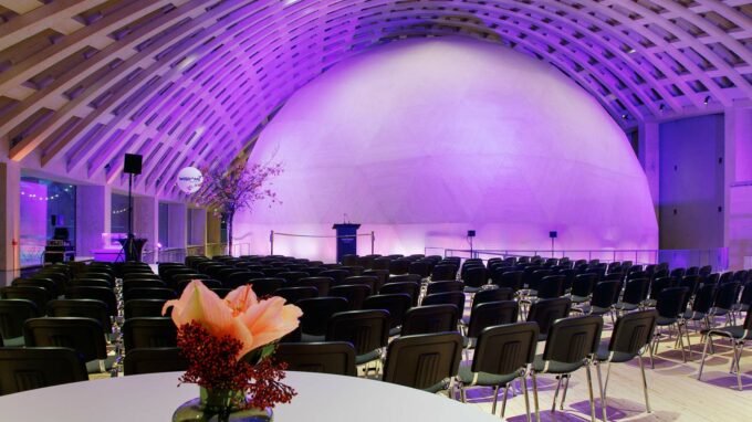 en rund dome som visas i bakgrunden upplyst av lila. Framför finns svarta stolar uppradade.