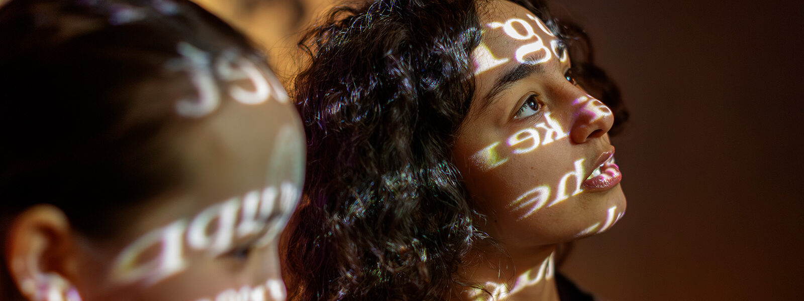 Two girls looking in awe at a video on a monitor. The monitors lights are reflected on their faces.