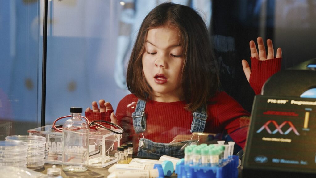 Flicka trycker ansiktet mot monter med labbutrustning