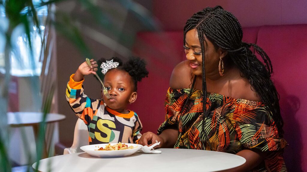 en flicka som äter nöjt sin tallrik mat medan mamma tittar på.