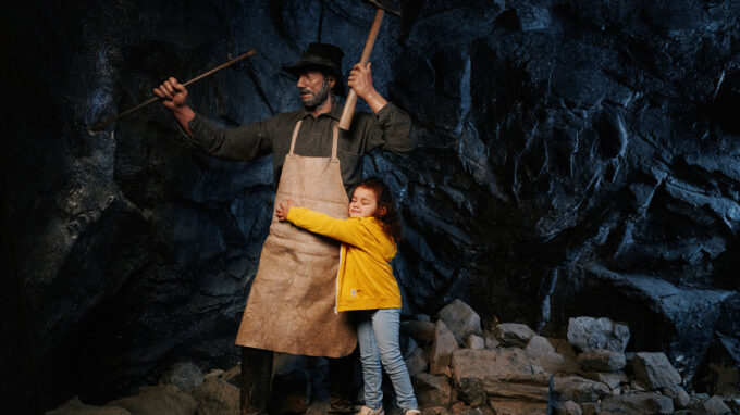 litet barn kramar om en vaxdocka som föreställer en gruvarbetare