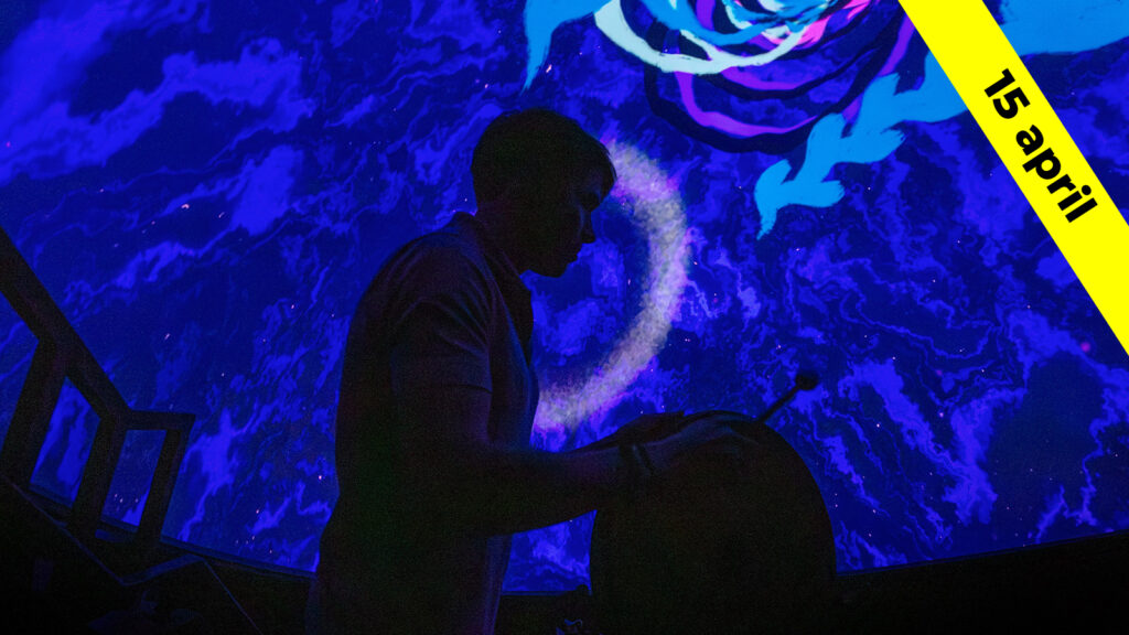 Man som spelar på trummor i neonljus framför en audiovisuell projektion.