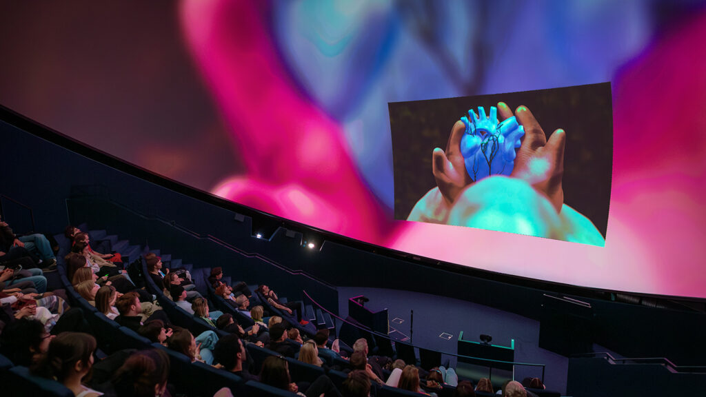 publik som tittar på en hand och hjärta som projiceras upp på stor skärm