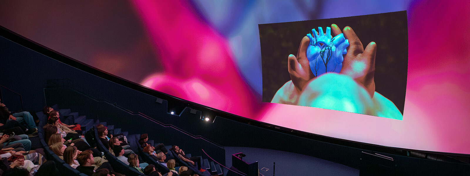 publik som tittar på en hand och hjärta som projiceras upp på stor skärm