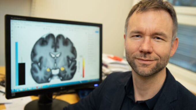 Man som ler mot kameran. I bakgrunden skymtas röntgenbild på en hjärna.
